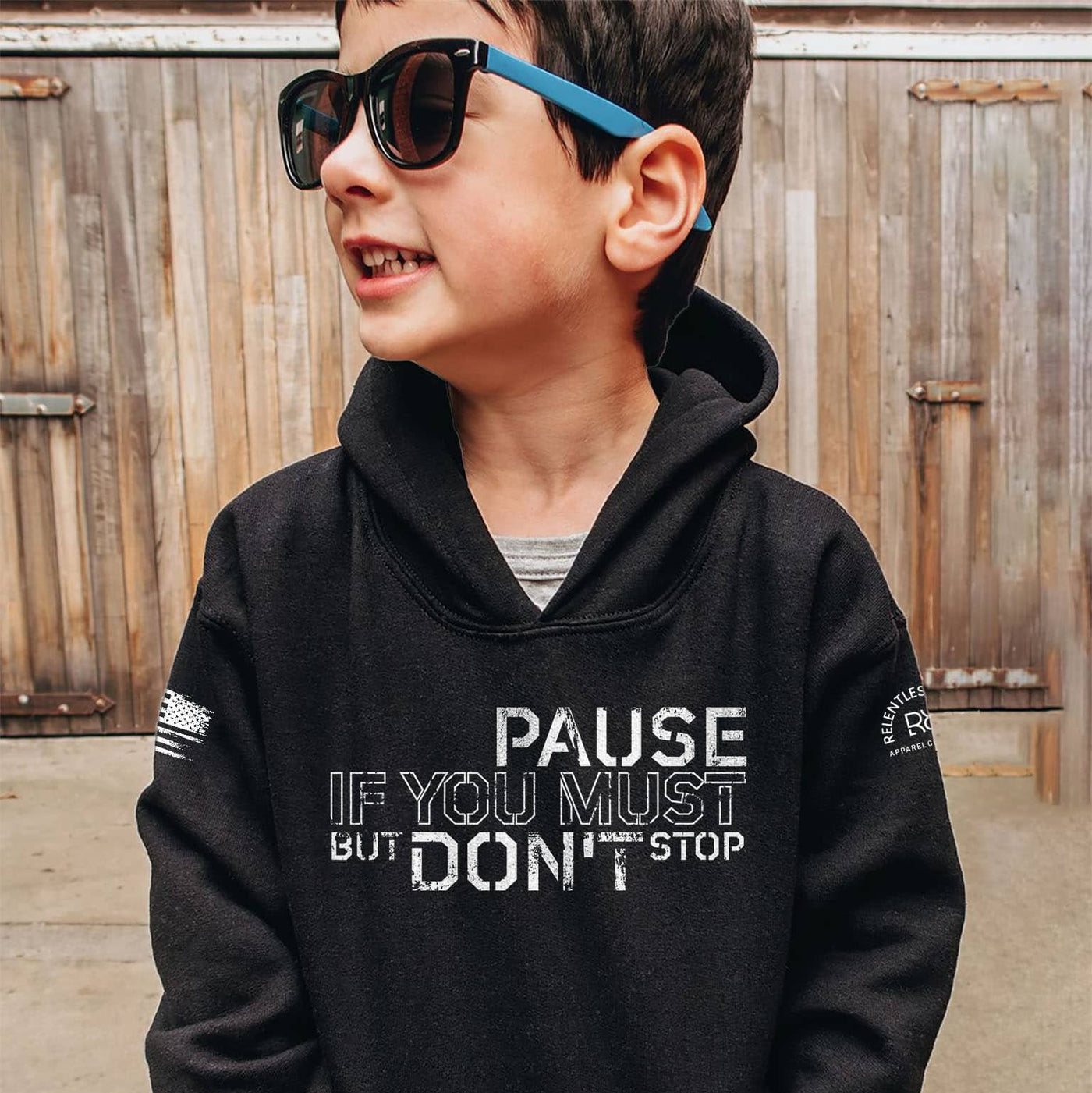 Child wearing a black hoodie with text, standing in front of a wooden fence.