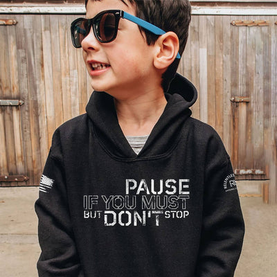 Child wearing a black hoodie with text, standing in front of a wooden fence.
