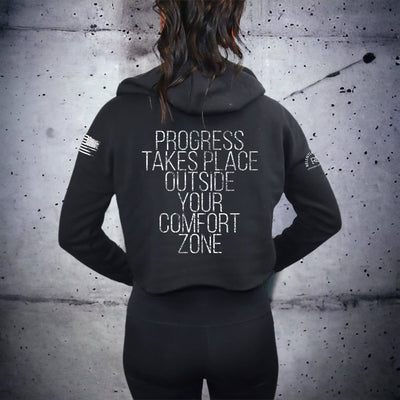 Person wearing a black hoodie with a motivational quote on the back against a textured wall.