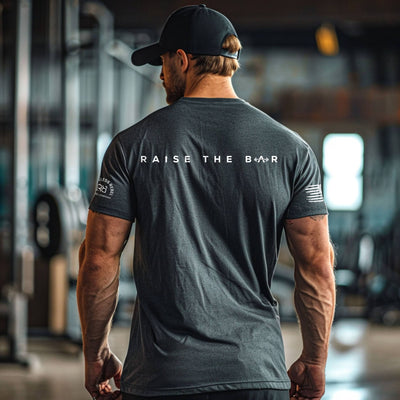 Man wearing a gray t-shirt with 'Raise The Bar' text in a gym setting