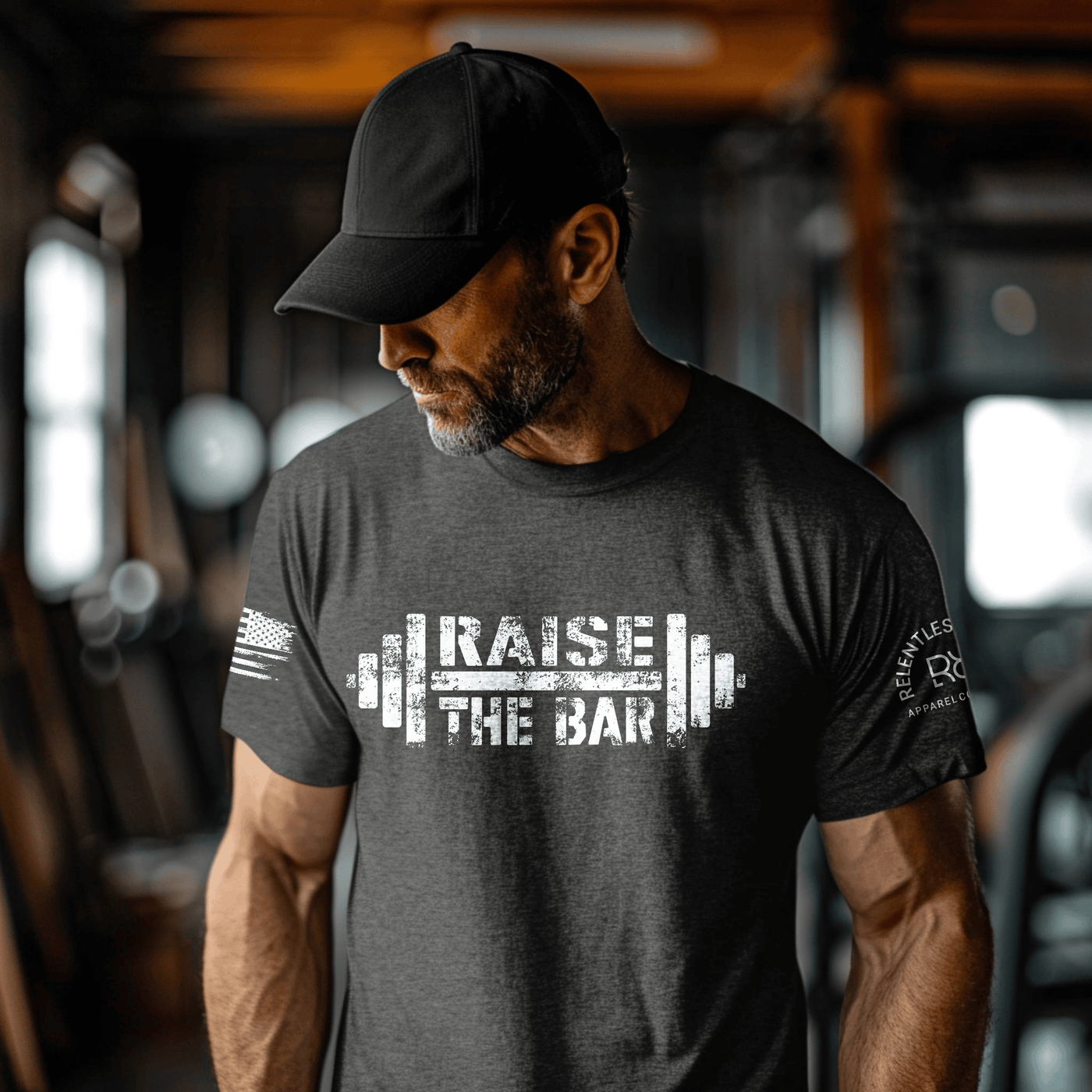 Man wearing a dark gray t-shirt with 'Raise the Bar' graphic and text in a gym setting