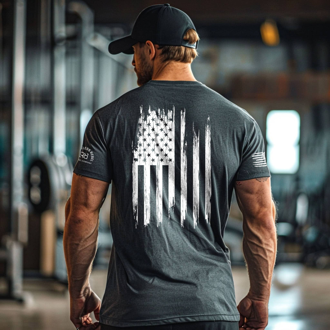 Man wearing a dark gray t-shirt with an American flag design, standing in a gym.