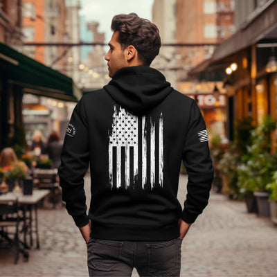 Man wearing a black hoodie with an American flag design outdoors.