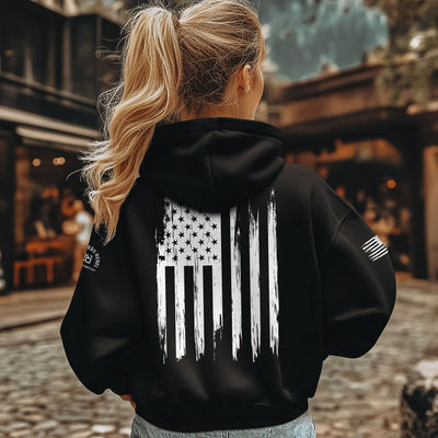 Person wearing a black hoodie with an American flag design outdoors
