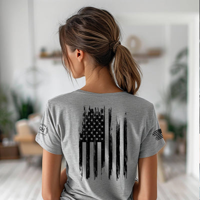 Person wearing a gray t-shirt with an American flag design on the back, standing in a blurred indoor setting.