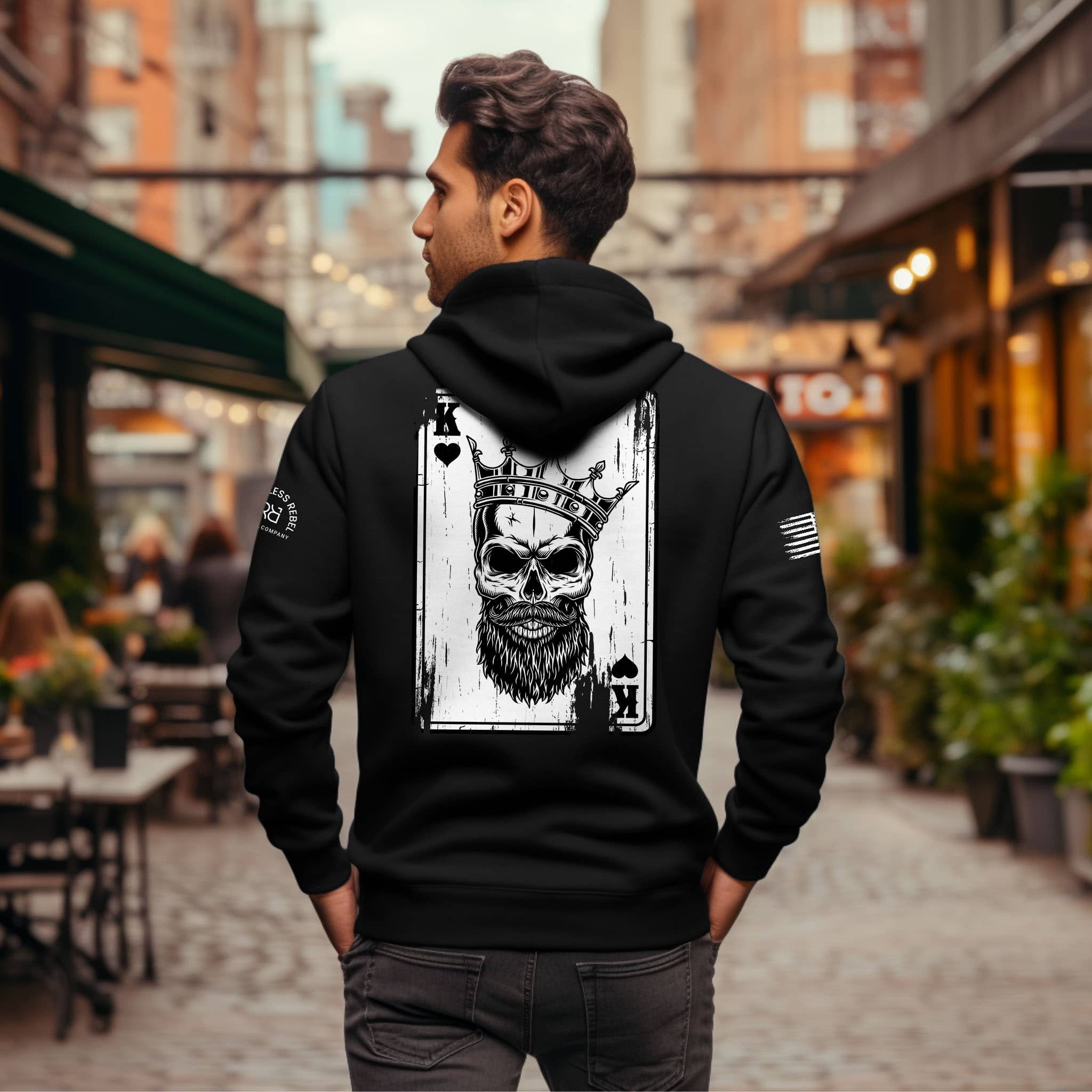 Man wearing a black hoodie with a skull and card design on the back, standing in an urban setting.