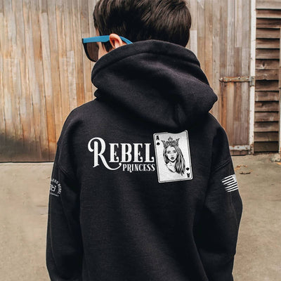 Person wearing a black hoodie with 'Rebel Princess' design on the back, standing in front of wooden panels.