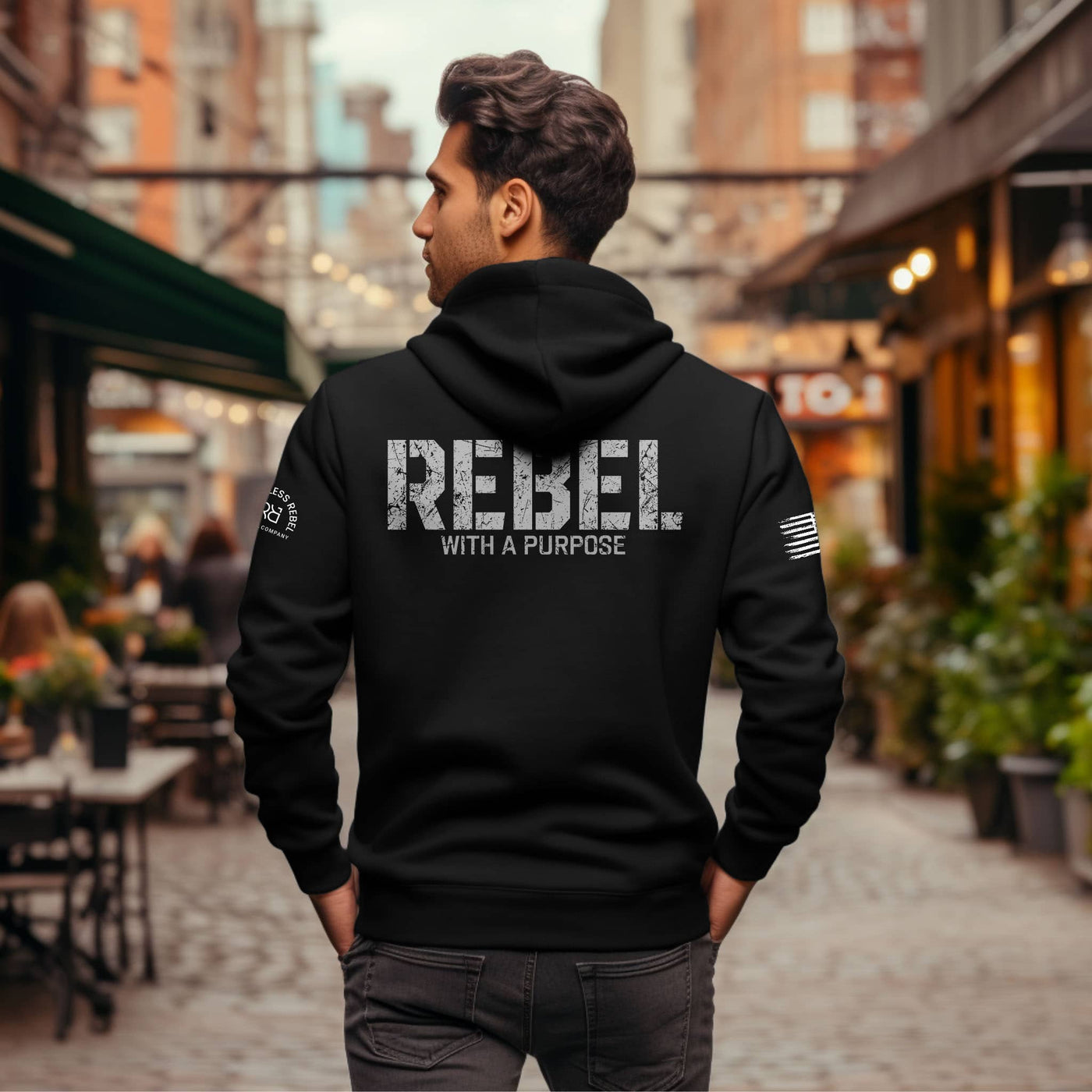 Person wearing a black hoodie with 'REBEL WITH A PURPOSE' text on the back, standing in an urban setting.
