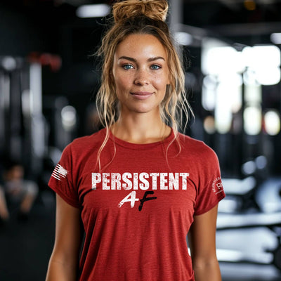Woman wearing a red t-shirt with 'PERSISTENT AF' text in a gym setting