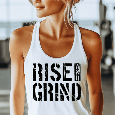 Woman wearing a white tank top with 'RISE & GRIND' text in a gym setting