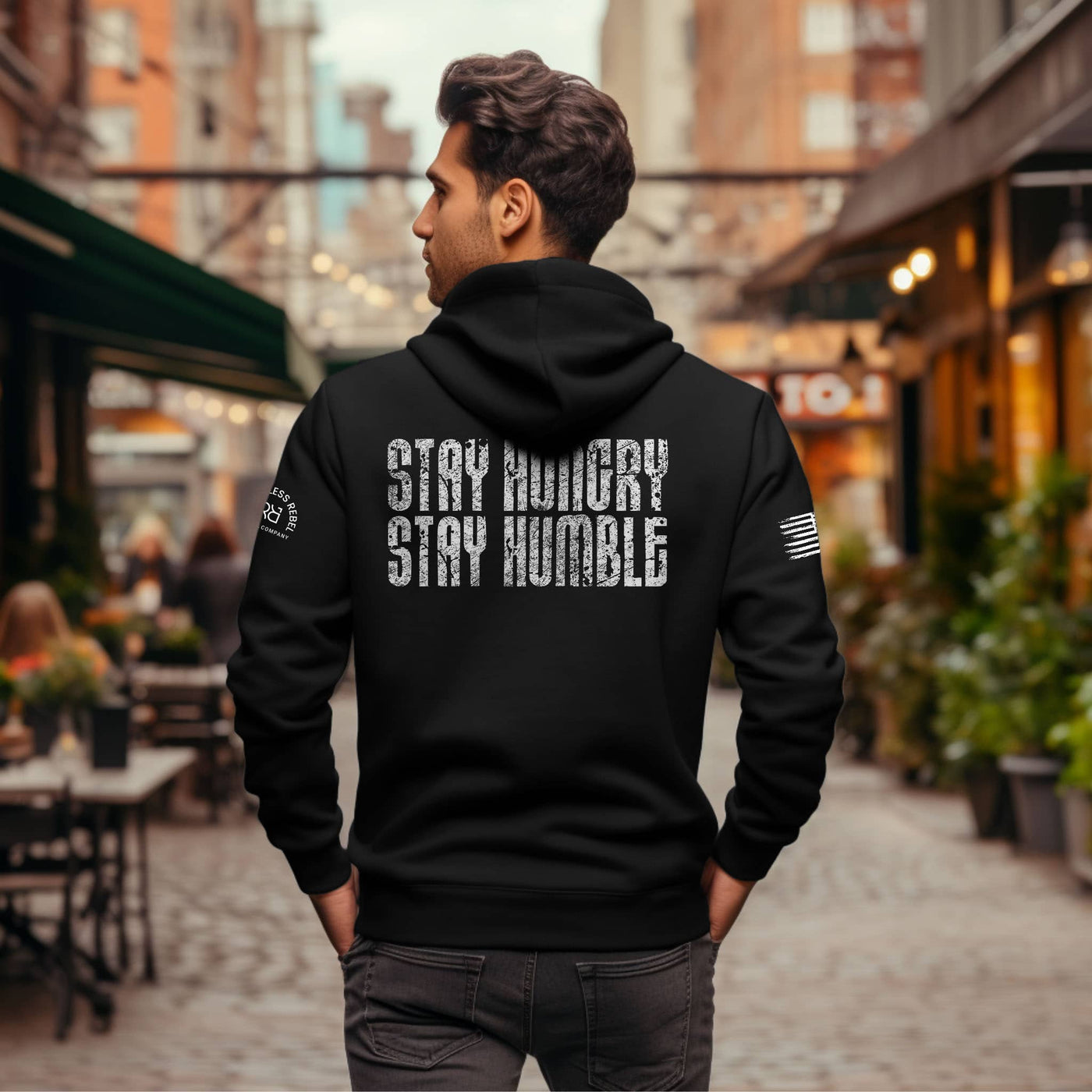 Man wearing a black hoodie with 'Stay Hungry Stay Humble' text on the back in an urban setting.