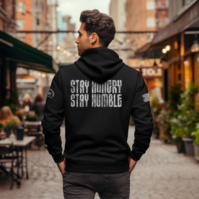 Man wearing a black hoodie with 'Stay Hungry Stay Humble' text on the back in an urban setting.