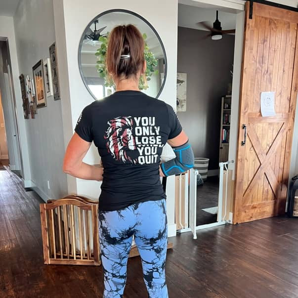 Person wearing a black t-shirt with text and blue leggings in a home setting.