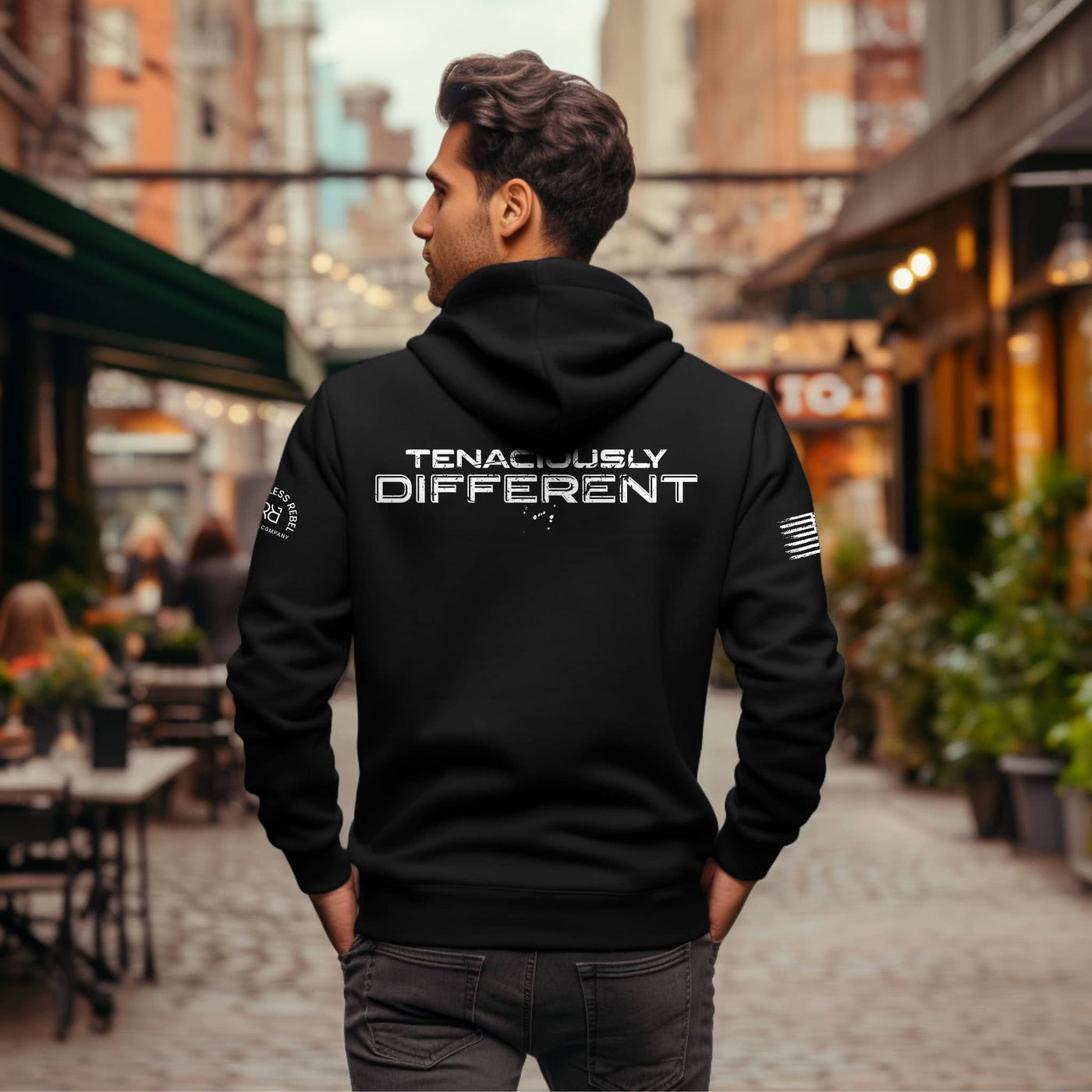 Man wearing a black hoodie with 'TENACIOUSLY DIFFERENT' text on the back, standing in an urban setting.
