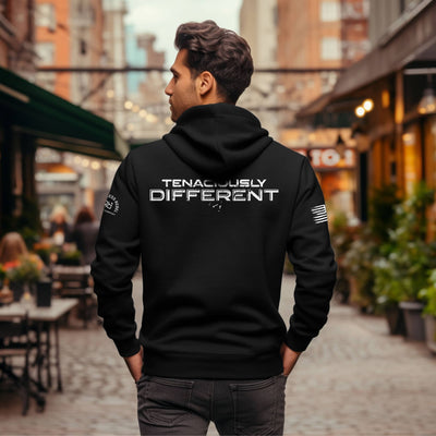 Man wearing a black hoodie with 'TENACIOUSLY DIFFERENT' text on the back, standing in an urban setting.