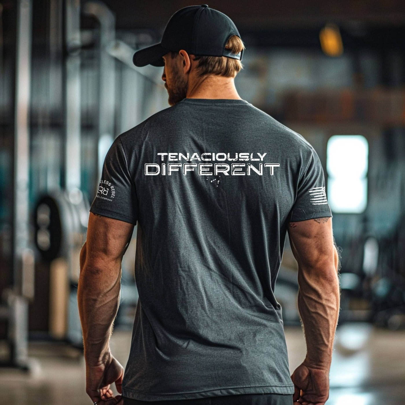 Man wearing a black t-shirt with 'TENACIOUSLY DIFFERENT' text in a gym setting
