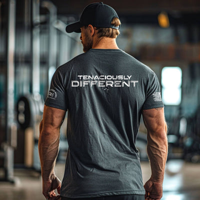 Man wearing a black t-shirt with 'TENACIOUSLY DIFFERENT' text in a gym setting