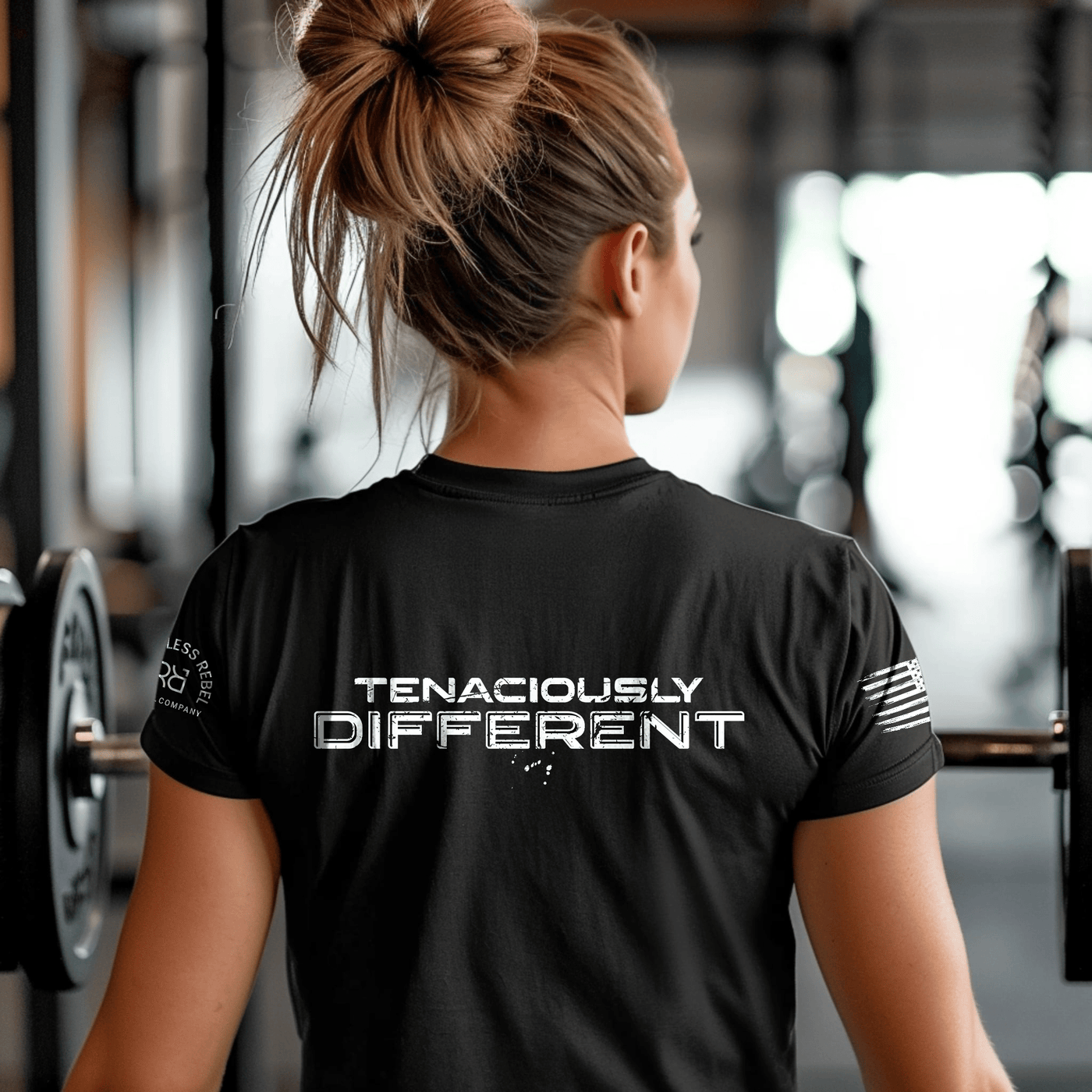 Person wearing a black t-shirt with 'Tenaciously Different' text in a gym setting
