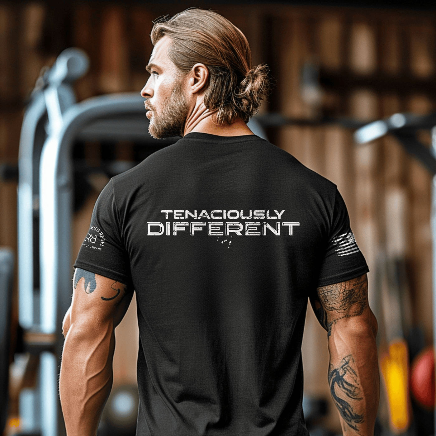 Man wearing a black tee in a gym setting with Tenaciously Different written on the back
