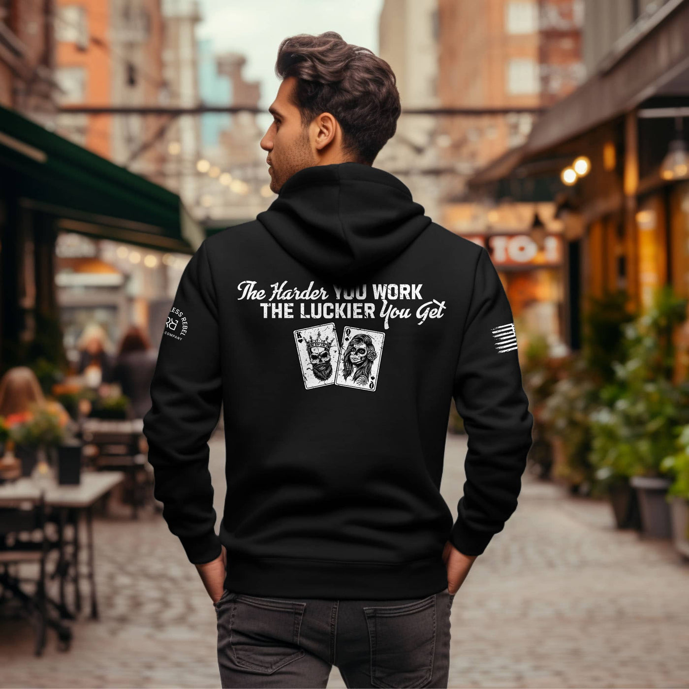 Man wearing a black hoodie with motivational quote and card design on the back, standing in an urban setting.