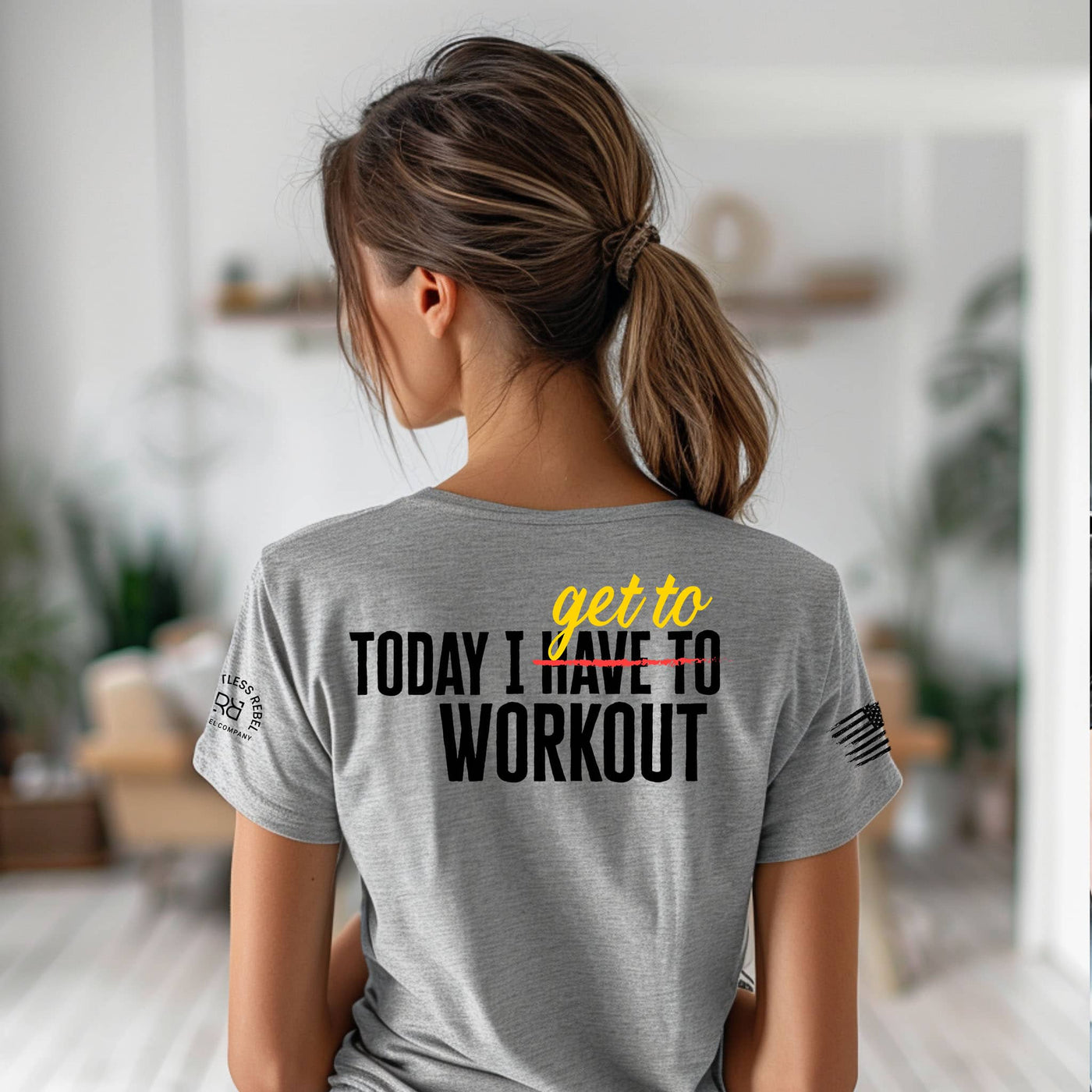 Person wearing a gray t-shirt with a motivational quote on the back in a home setting.