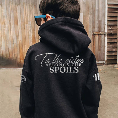 Person wearing a black hoodie with text on the back, standing in front of a wooden wall.