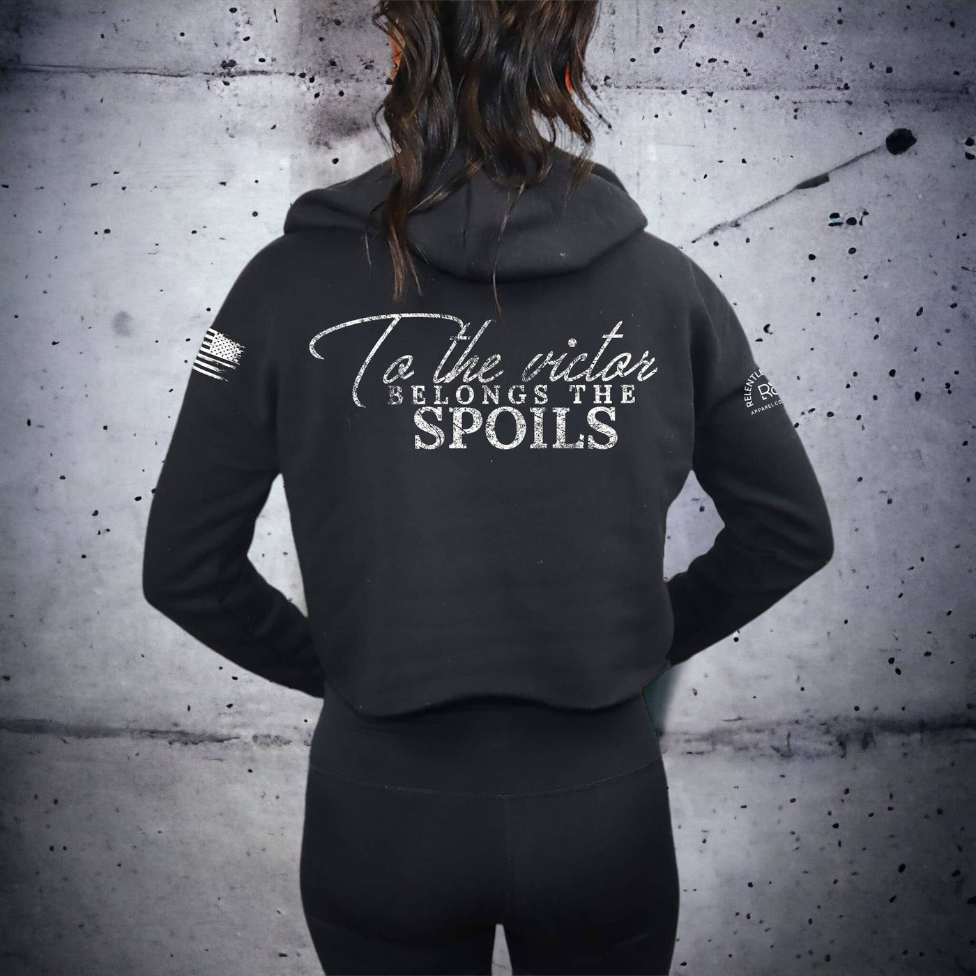 Person wearing a black hoodie with text on the back against a textured wall.
