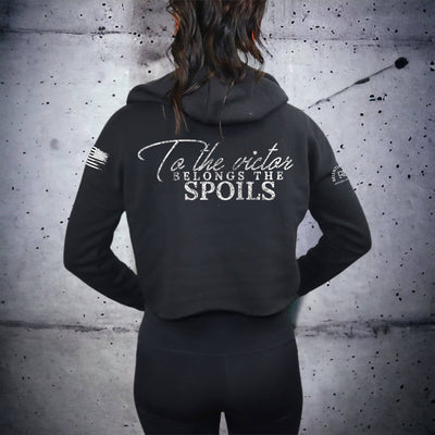Person wearing a black hoodie with text on the back against a textured wall.