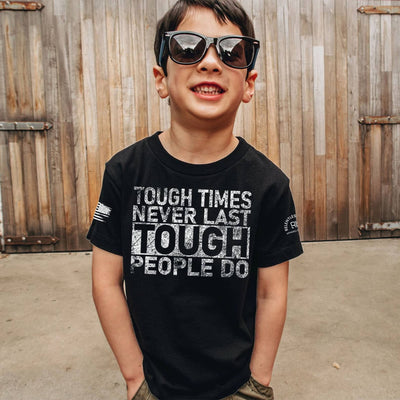 Child wearing sunglasses and a black t-shirt with motivational quote in front of wooden shutters.