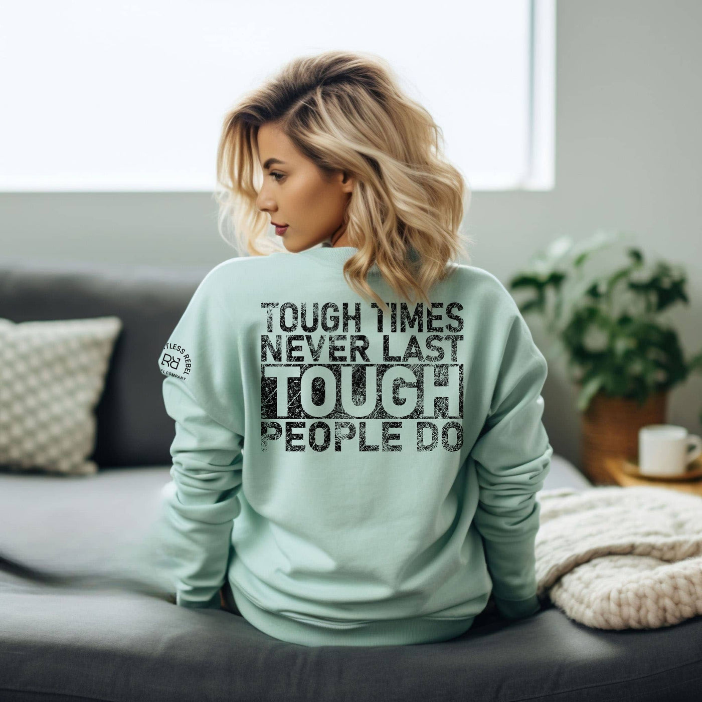 Woman wearing a light green sweatshirt with motivational text in a cozy living room.