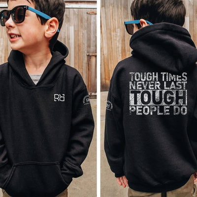 Child wearing a black hoodie with a motivational quote on the back, standing in front of a wooden fence.