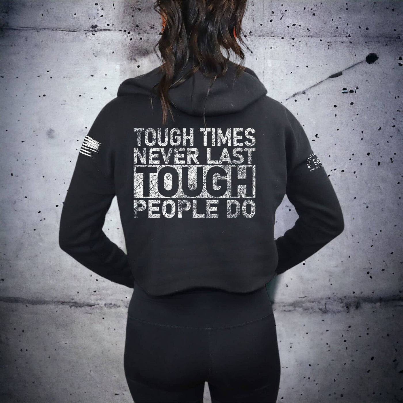Person wearing a black hoodie with motivational text on the back against a textured wall.