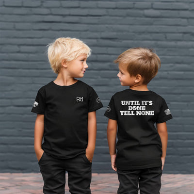 Two children wearing black t-shirts with text and logos against a brick wall.