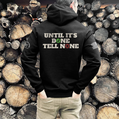 Person wearing a black hoodie with text on the back standing in front of stacked wooden logs.