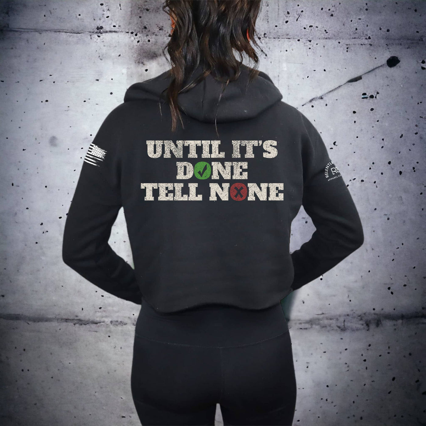 Person wearing a black hoodie with text on the back against a textured gray wall.