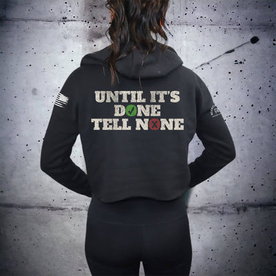 Person wearing a black hoodie with text on the back against a textured gray wall.