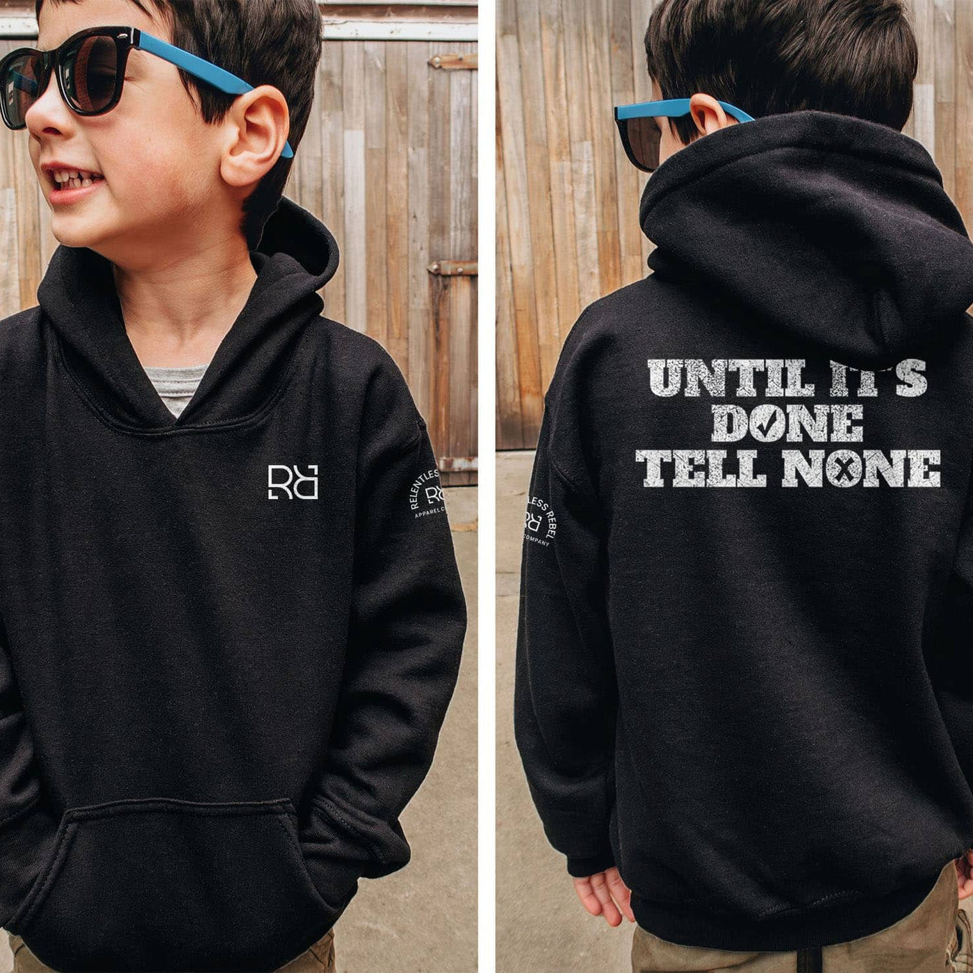 Child wearing a black hoodie with a logo on the front and text on the back, standing in front of a wooden fence.