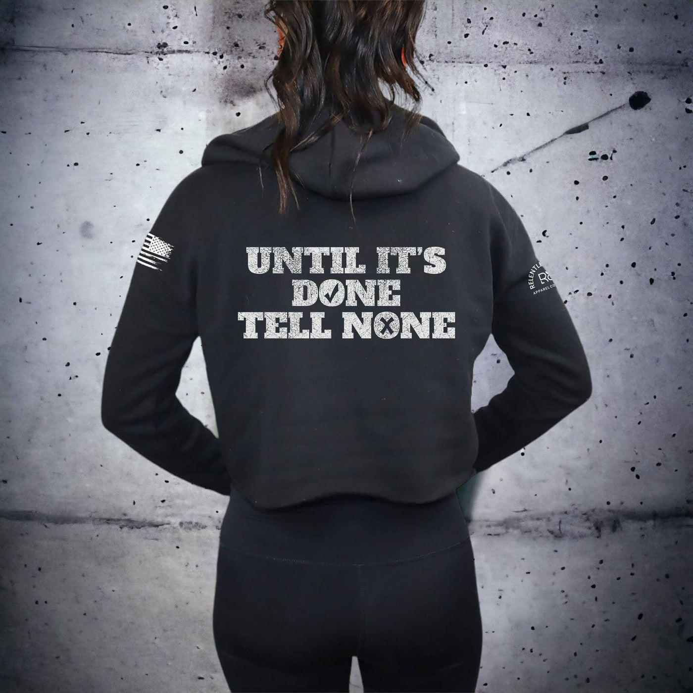 Person wearing a black hoodie with text on the back against a textured gray wall.