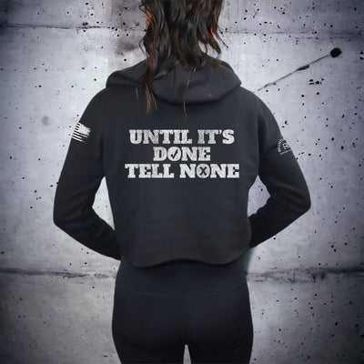 Person wearing a black hoodie with text on the back against a textured gray wall.