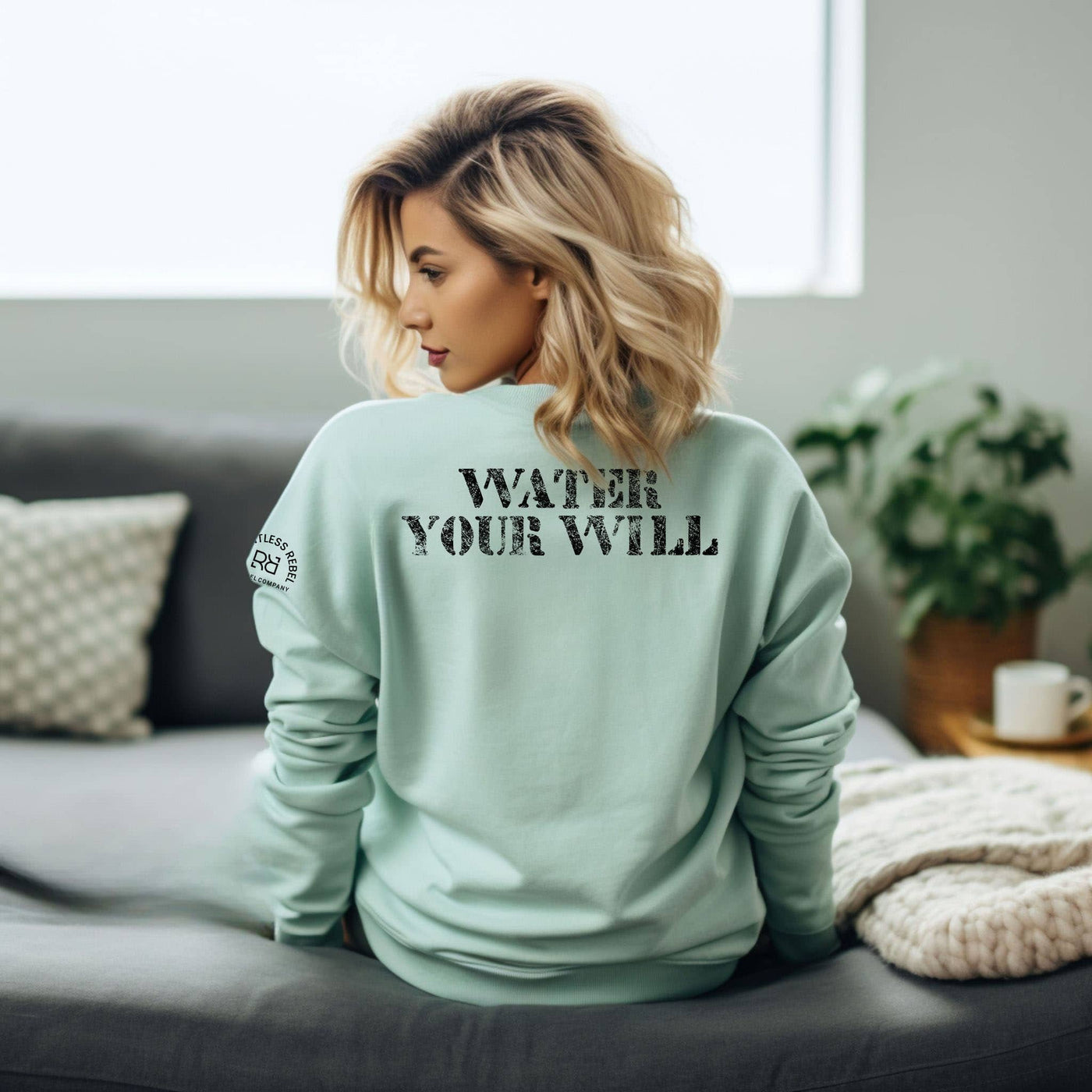 Woman wearing a light green sweatshirt with text on the back, sitting on a couch in a living room.