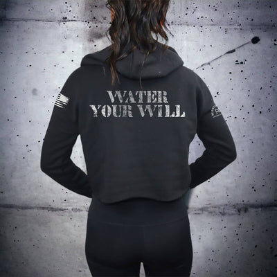 Person wearing a black hoodie with 'Water Your Will' text on the back against a textured gray wall.