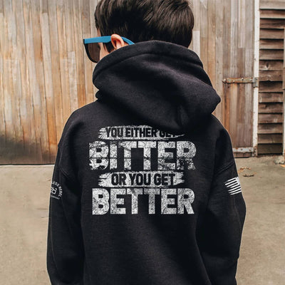Person wearing a black hoodie with motivational text on the back, standing in front of a wooden wall.
