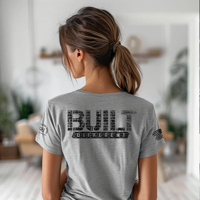 Person wearing a gray t-shirt with 'BUILT Different' text on the back in a blurred indoor setting