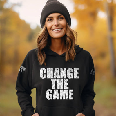 Woman wearing a black hoodie with 'CHANGE THE GAME' text in an autumn forest setting