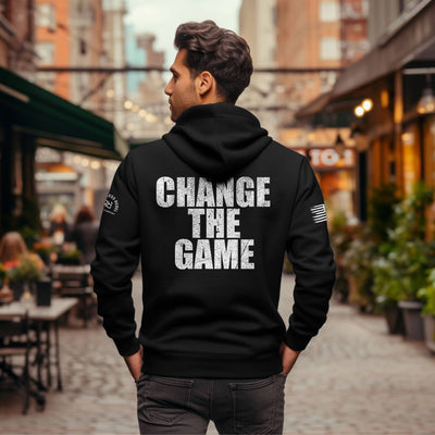 Person wearing a black hoodie with 'CHANGE THE GAME' text on the back in an urban setting.