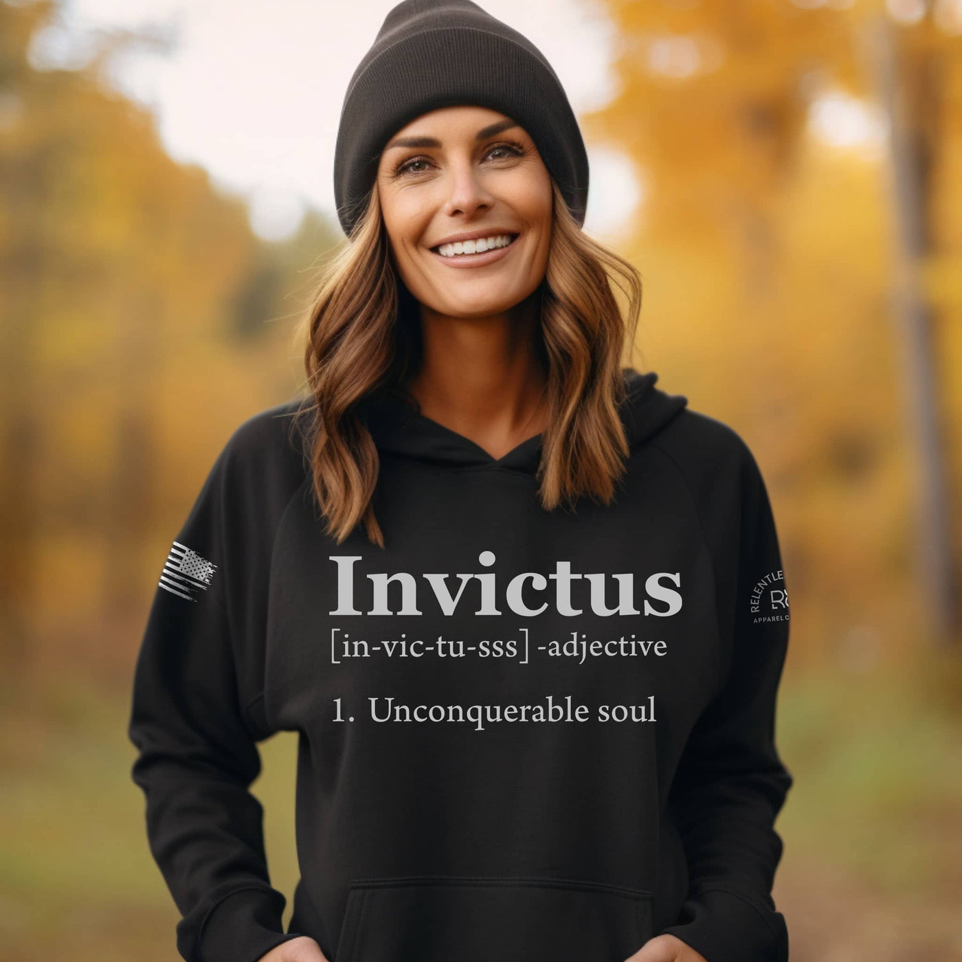Woman wearing a black hoodie with 'Invictus' text in an autumn setting