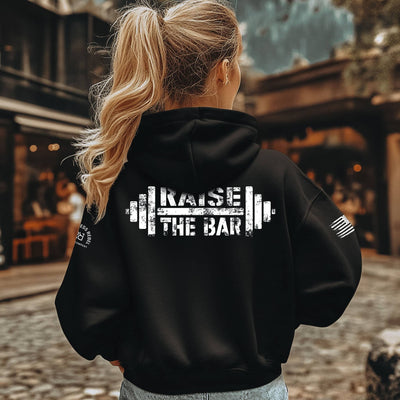 Person wearing a black hoodie with 'Raise the Bar' text on the back, standing outdoors.