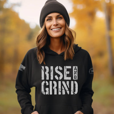 Woman wearing a black hoodie with 'Rise & Grind' text in an autumn setting