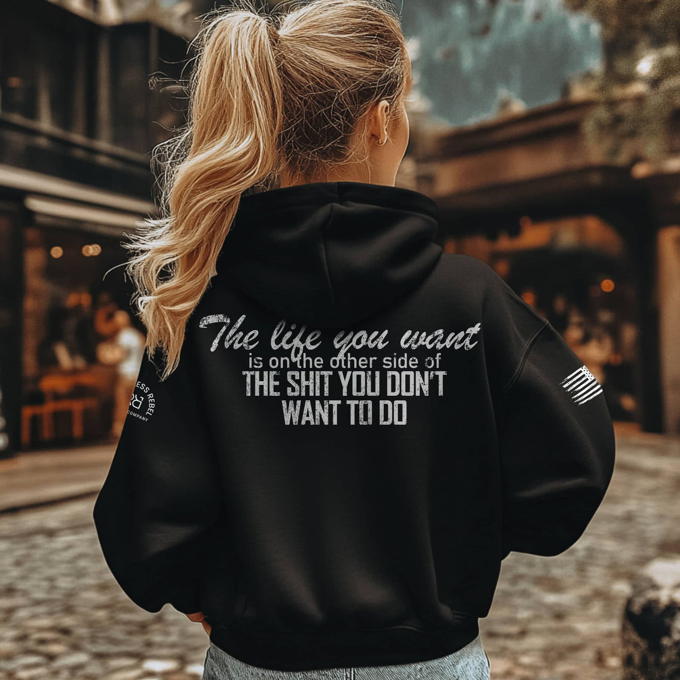 Person wearing a black hoodie with a motivational quote on the back, standing outdoors.