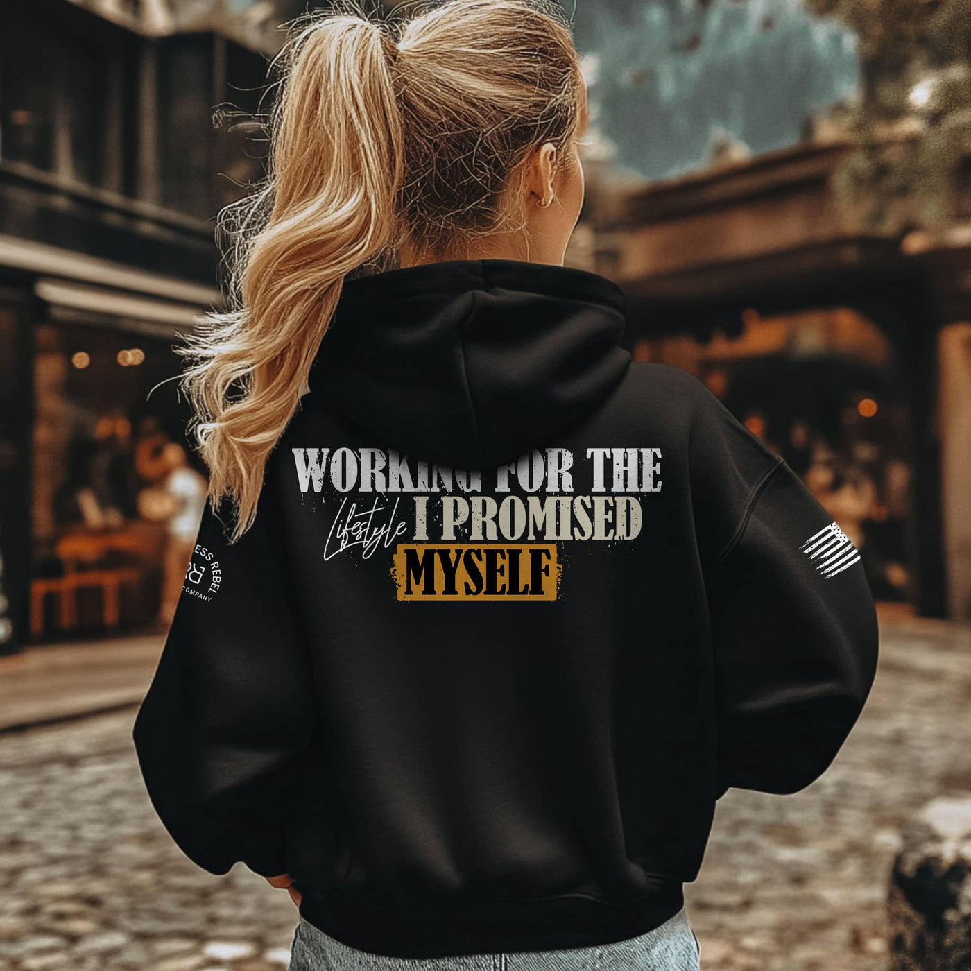 Person wearing a black hoodie with text on the back, standing outdoors.